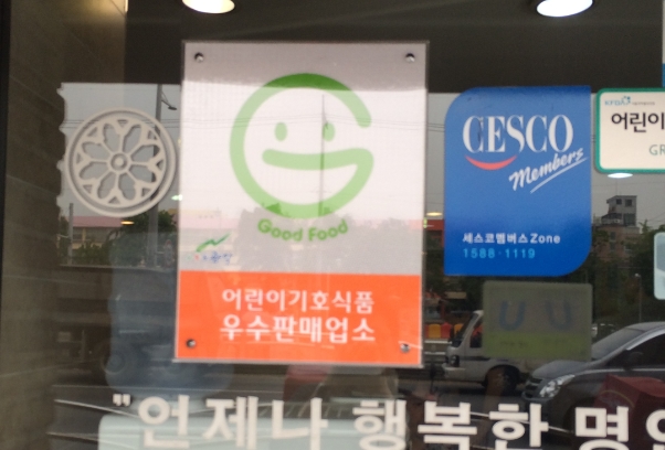 'Good Food'라고 적힌 웃는 얼굴 모양의 마크가 있는 어린이기호식품 우수판매업소 표시의 예