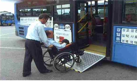 휠체어를 탄 사람이 버스 운전기사님의 도움을 받아 저상버스에 탑승하는 그림입니다.